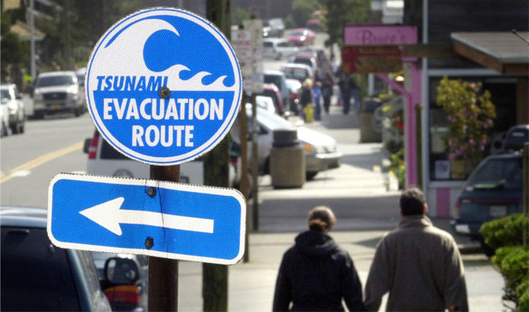 A couple walks hand in hand past one of many tsunami evacuation route signs in Cannon Beach, Ore., Friday, April 1, 2005. (AP Photo/Don Ryan)