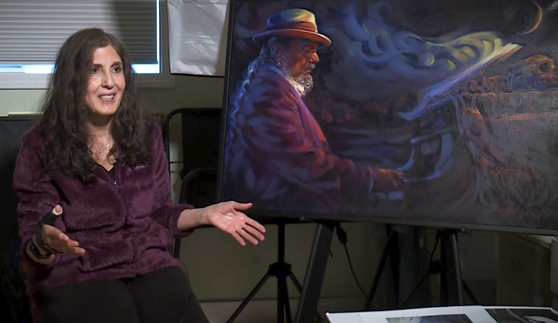 Portland artist Diane Russell sits next to a portrait she did of Dr. John, November 2022 (KOIN)