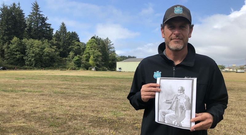 Jesse Dolin with the Oregon Coast Visitors Association holds a picture of Louis Southworth in the spot where the Louis Southworth Park will be built in Waldport by 2024 (City of Waldport)