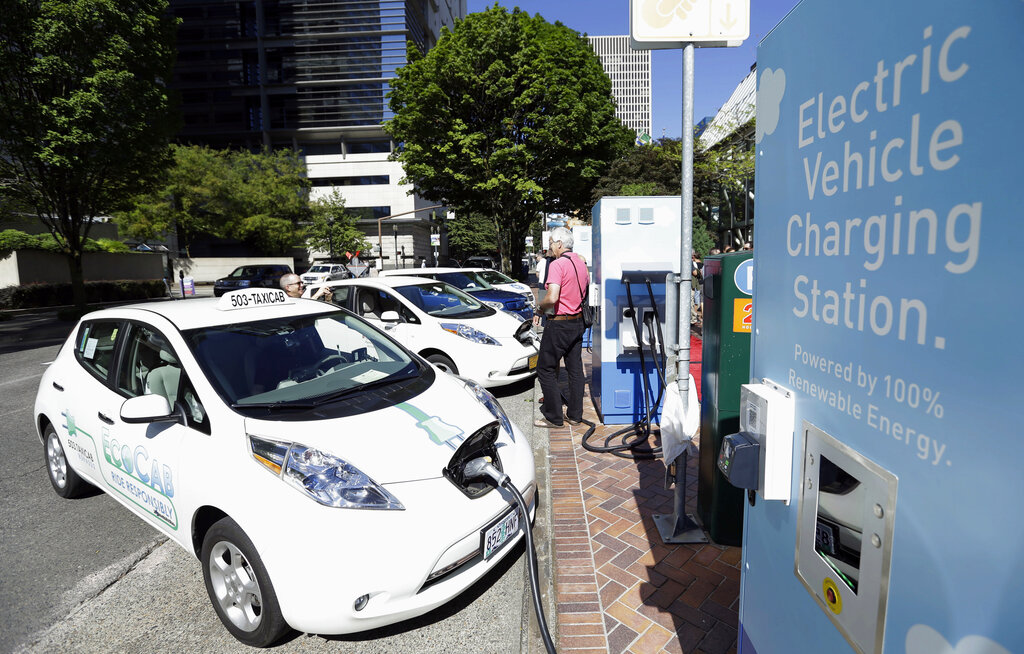 FILE - A line of electric cars and newly installed charging stations sit in front of the Portland General Electric headquarters building on July 28, 2015, in Portland, Ore. Policymakers for the Oregon Department of Environmental Quality on Monday, Dec. 19, 2022, approved a rule that prohibits the sale of new gasoline-powered passenger vehicles in Oregon by 2035. (AP Photo/Don Ryan, File)