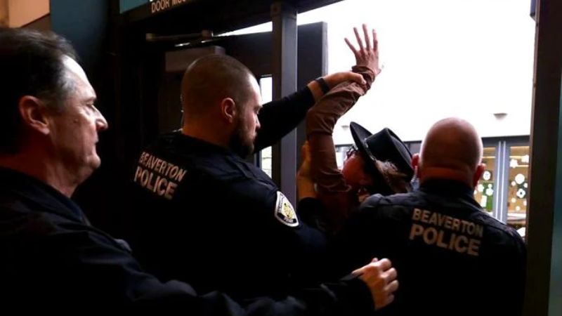 A woman is escorted out of Conestoga Recreation and Aquatic Center in Beaverton by law enforcement after confronting Sen. Ron Wyden during a town hall meeting