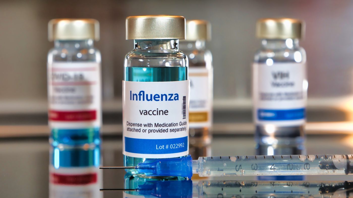 Bottles of influenza vaccine. Bottles with a syringe on black table and stainless steel background.