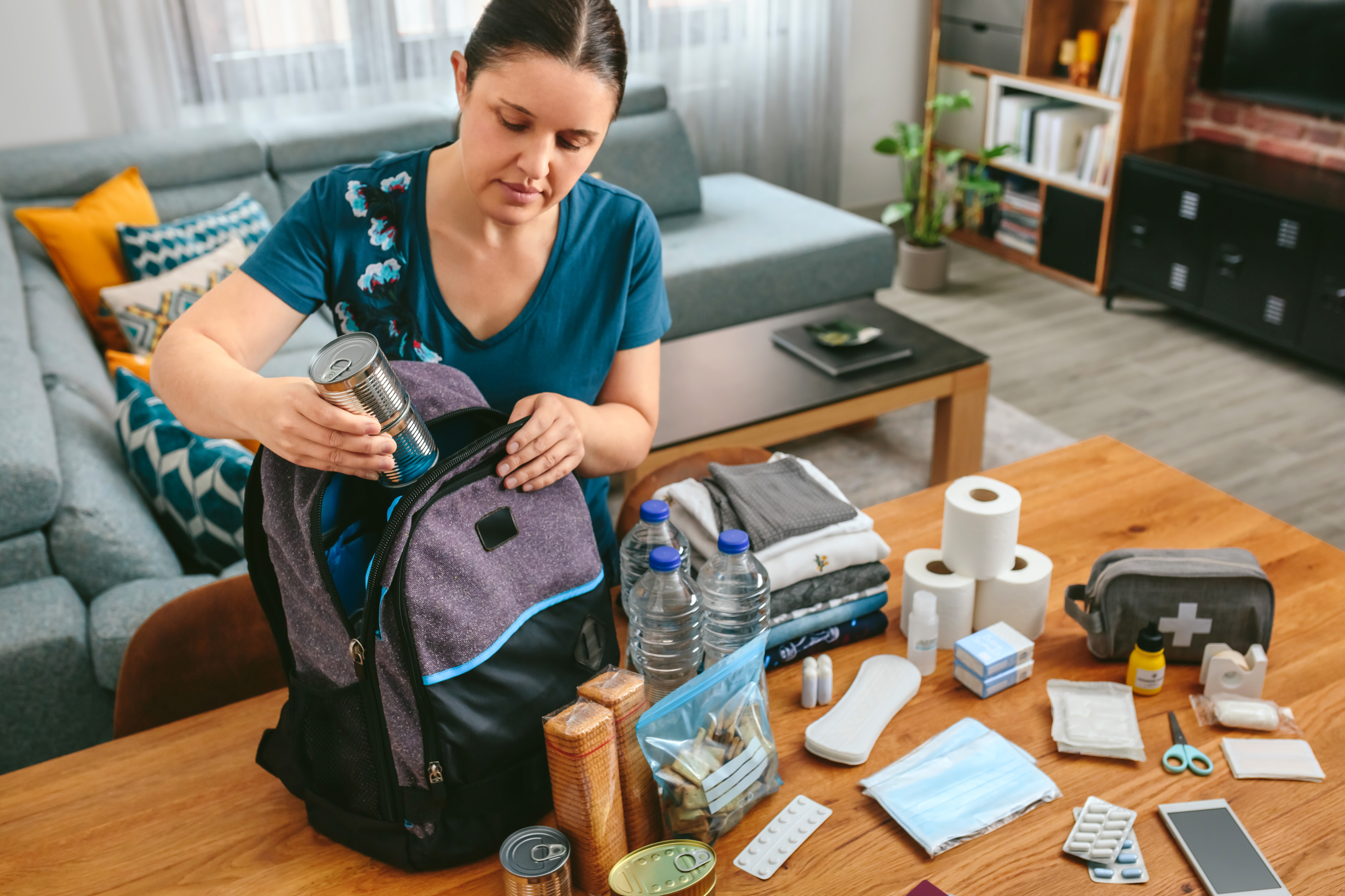 A woman puts cans of food in a backpack to prepare an emergency survival kit. (Getty)