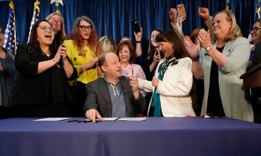 Colorado Gov. Jared Polis, front center, is applauded by, state Sen. Julie Gonzales, far left, state Rep. Brianna Titone, second from left, Lt. Gov. Dianne Primavera, third from left, state Sen. Sonya Jaquez Lewis and state Rep. Meg Froelich after he signed the first of three bills that enshrined protections for abortion and gender-affirming care procedures and medications during a ceremony with bill sponsors and supporters, Friday, April 14, 2023, in the State Capitol in Denver. (AP Photo/David Zalubowski)