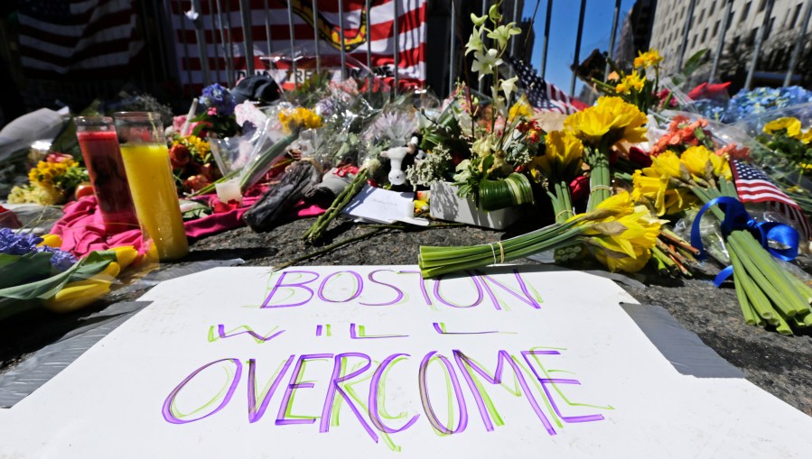 Flowers and signs adorn a barrier, two days after two explosions killed three and injured hundreds, near the of finish line of the Boston Marathon at a makeshift memorial for victims and survivors of the bombing, April 17, 2013, in Boston. The 10th anniversary of the Boston Marathon bombing on April 17, 2023 will be marked with a wreath laying at the finish line to remember those who were killed, a day of community service and an event for the public to gather to reflect on the tragedy. (AP Photo/Charles Krupa, File)