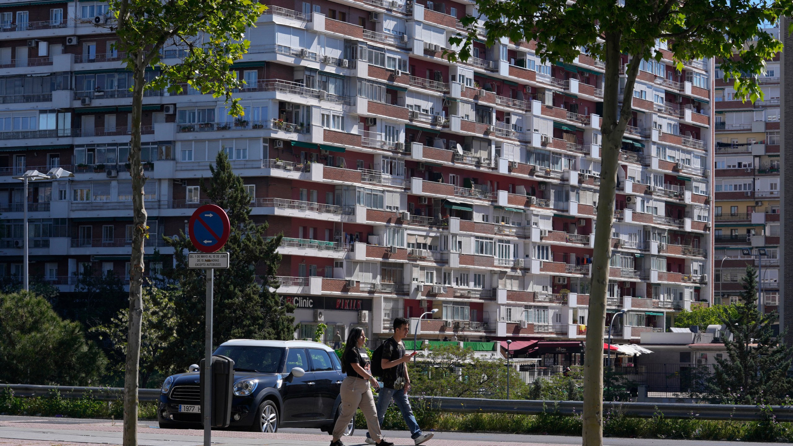 A young couple walk in front of housing blocks in Madrid, Spain, Tuesday, April 18, 2023. Spain's leftist coalition government has approved a plan to make available some 50,000 houses for rent at affordable prices as part of measures aimed at curbing soaring rents and house prices.The apartments will come from the state-controlled SAREB 'bad bank' that was set up in 2012 to relieve troubled banks of their most toxic assets during the international financial crisis. (AP Photo/Paul White)