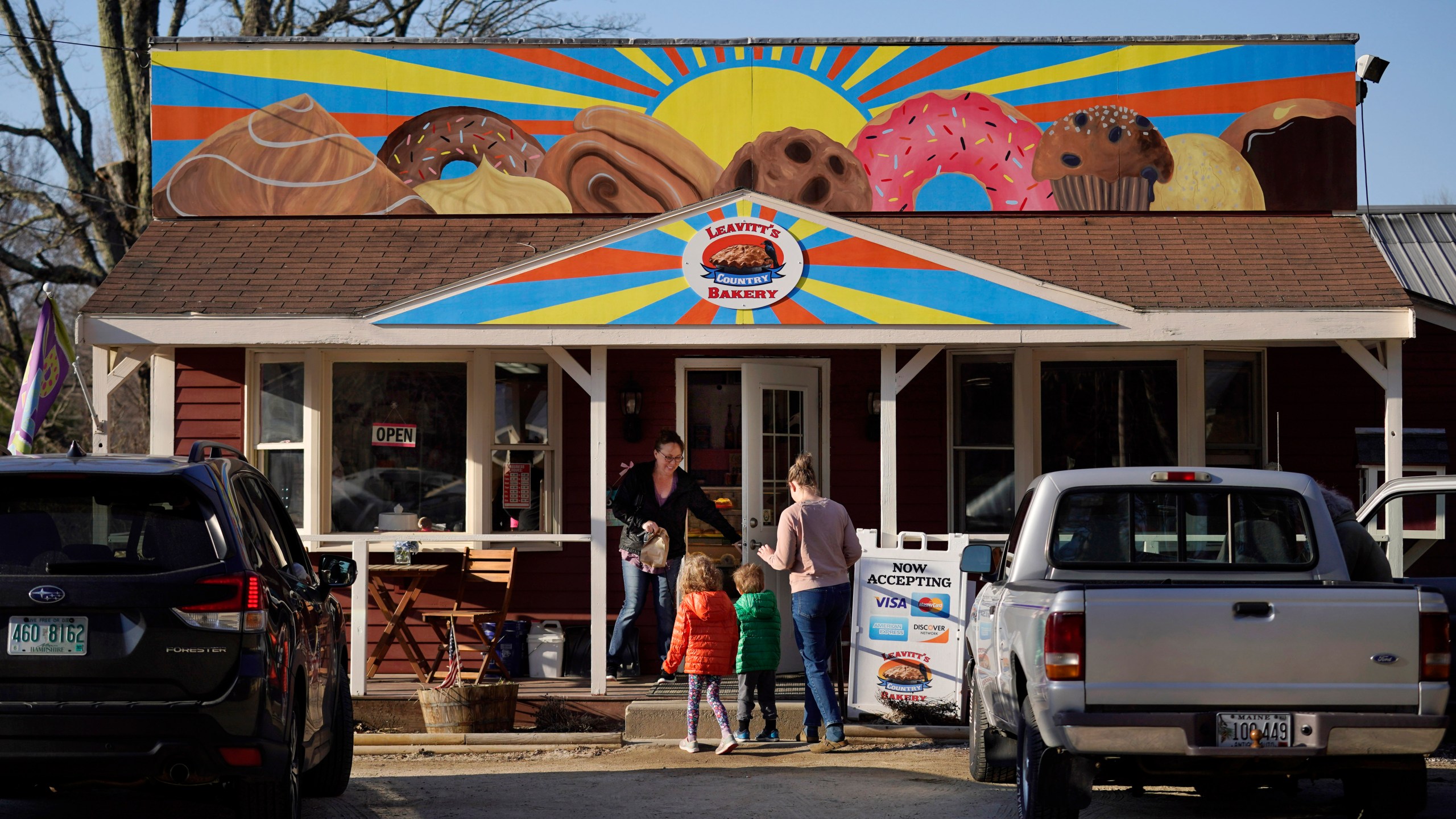 A customer holds the door for a family arriving at Leavitt's Country Bakery, Thursday, April 13, 2023, in Conway, N.H. The large painting of pastries created by students and displayed over the bakery is at the center of a legal battle pitting a zoning ordinance against freedom-of-speech rights. (AP Photo/Robert F. Bukaty)