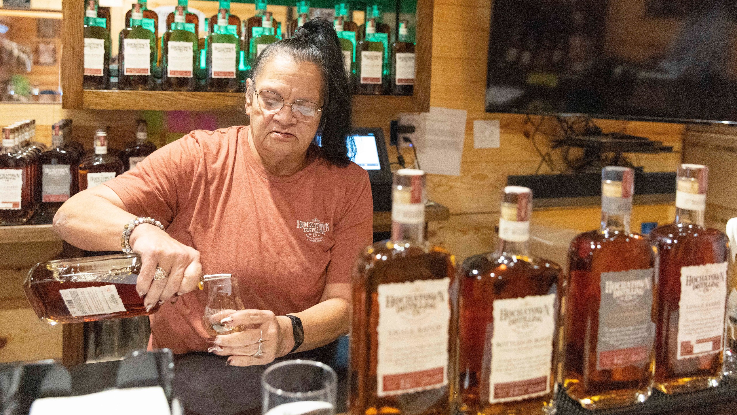 Bartender June Davis pours drinks inside the Hochatown Distilling Co. bar in Broken Bow, Okla. on Thursday, April 20, 2023. The growing optimism of McCurtain County's tourism boom over the last two decades took a gut punch last week when the local newspaper identified several county officials, including the sheriff and a county commissioner, who were caught on tape discussing killing journalists and lynching Black people. (AP Photo/Alonzo Adams)