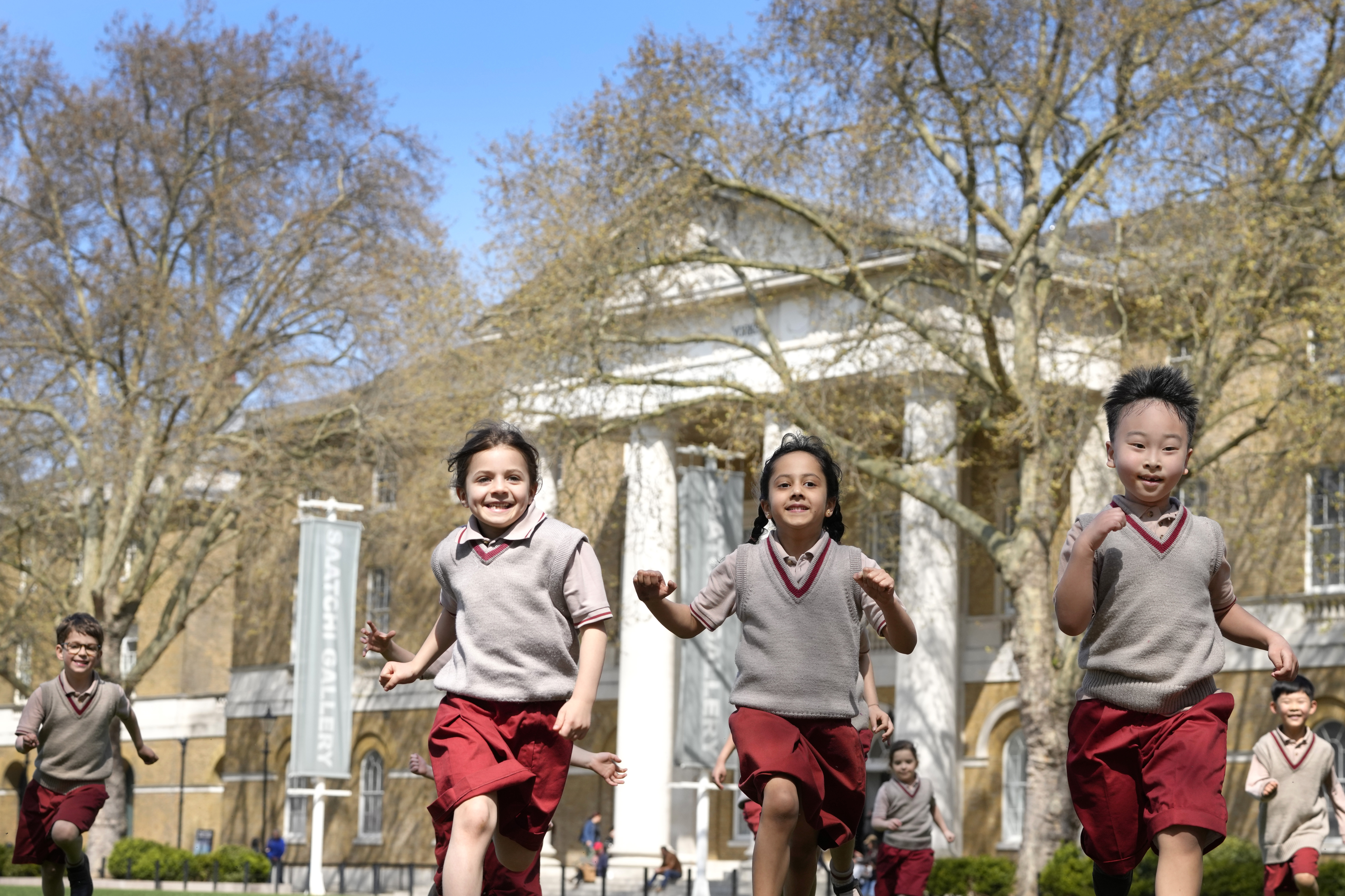 Pupils from Hill House School in London, play on the grass in front of the now Saatchi Gallery, where Britain's King Charles III played sport as a pupil, Thursday, April 20, 2023. King Charles III hasn’t even been crowned yet, but his name is already etched on the walls of Hill House School in London. A wooden slab just inside the front door records Nov. 7, 1956, as the day the future king enrolled at Hill House alongside other notable dates in the school’s 72-year history. (AP Photo/Kirsty Wigglesworth)