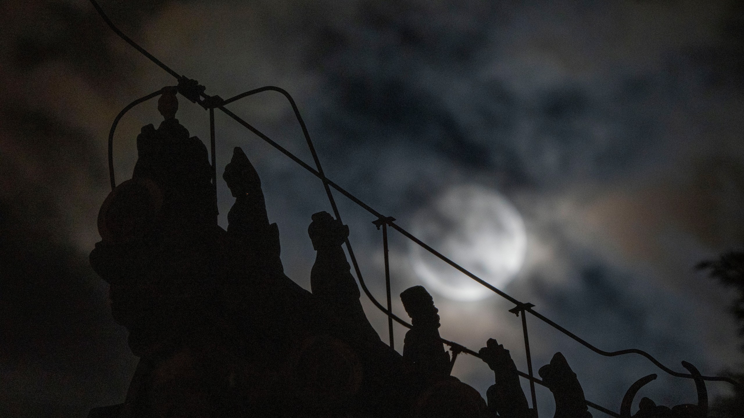 Roof decorations depicting mythical sacred beasts are silhouetted near a penumbral lunar eclipse partially blocked by clouds during the early hours of Saturday, May 6, 2023 in Beijing. (AP Photo/Ng Han Guan)