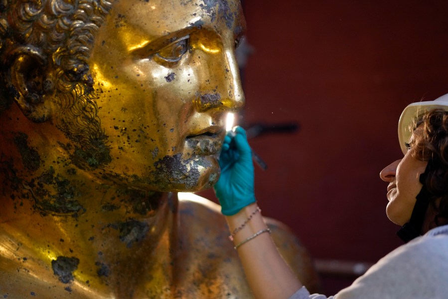 Vatican Museum restorer Alice Baltera works on the bronze Hercules statue, in the Round Hall of the Vatican Museums, Thursday, May 11, 2023. Work will continue until December to reveal the 4-meter- (13-foot-) tall Hercules, believed to have stood in ancient Rome’s Pompey Theater, to its original golden sheen. The discovery of the gilded bronze in 1864 during work on a banker’s villa near Piazza dei Fiori made global headlines. (AP Photo/Andrew Medichini)