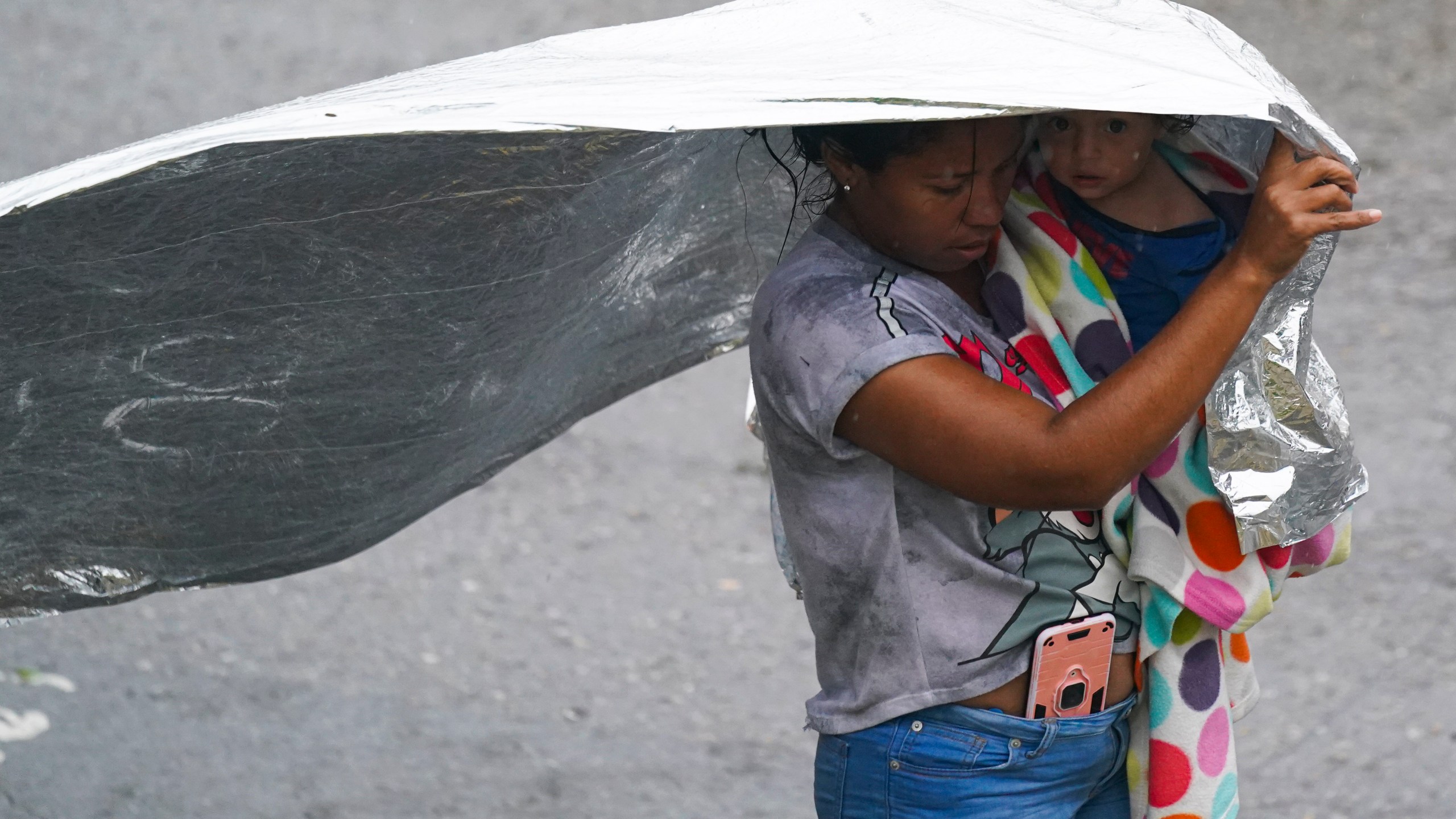 A Venezuelan migrant uses an emergency blanket as cover from the rain, near the banks of the Rio Grande in Matamoros, Mexico, Saturday, May 13, 2023. As the U.S. ended its pandemic-era immigration restrictions, migrants are adapting to new asylum rules and legal pathways meant to discourage illegal crossings. (AP Photo/Fernando Llano)