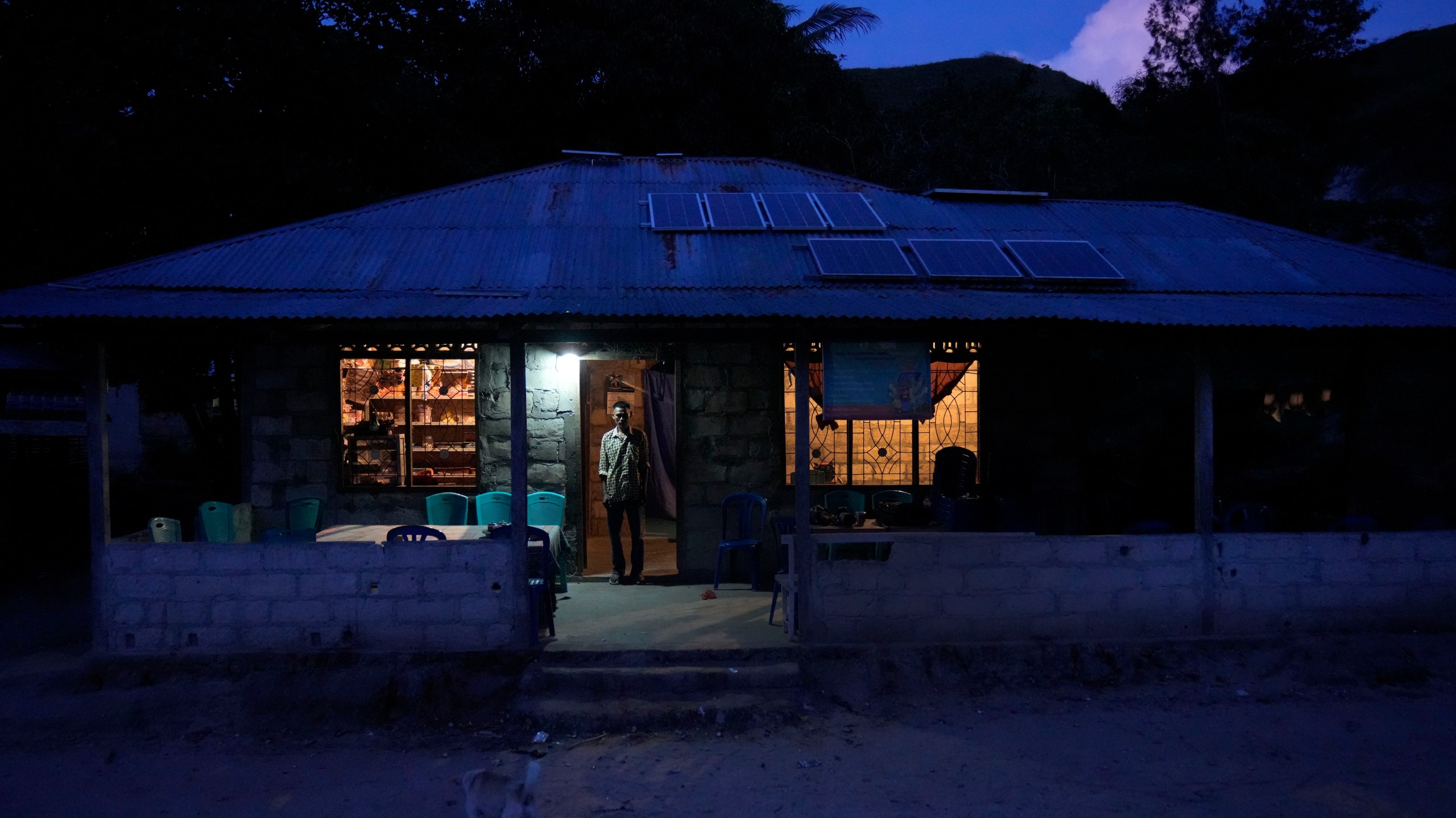 Bara Kilimandang stands at the door of his house whose electricity comes from solar energy in Walatungga on Sumba Island, Indonesia, Tuesday, March 21, 2023. In Indonesia's far-east island, off-grid solar is lighting up lives for residents still living out of reach of the country's national electricity provider. (AP Photo/Dita Alangkara)