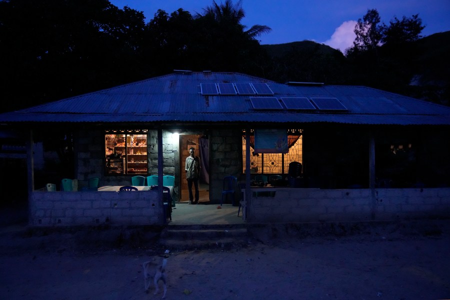 Bara Kilimandang stands at the door of his house whose electricity comes from solar energy in Walatungga on Sumba Island, Indonesia, Tuesday, March 21, 2023. In Indonesia's far-east island, off-grid solar is lighting up lives for residents still living out of reach of the country's national electricity provider. (AP Photo/Dita Alangkara)