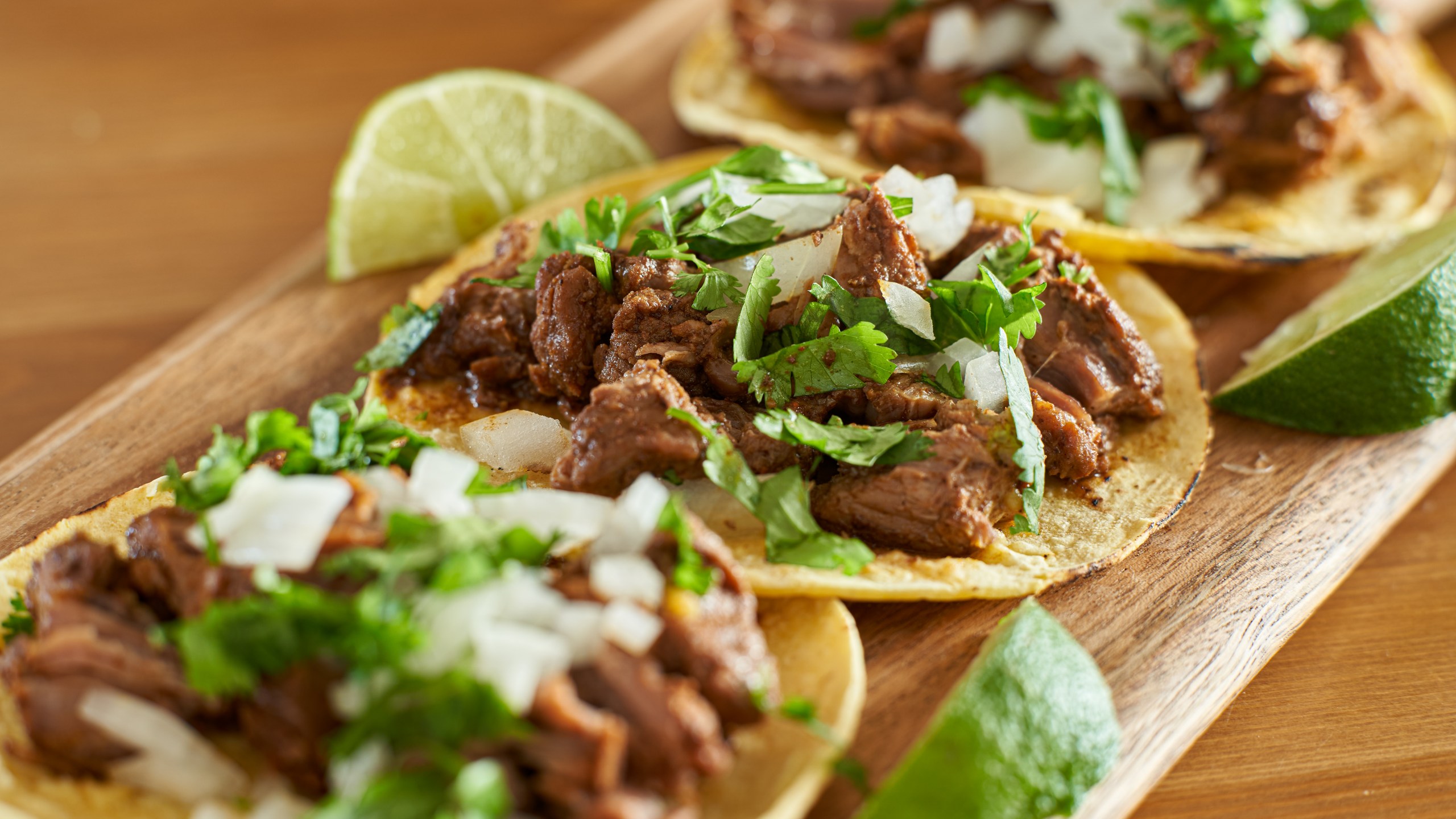 Three carne asada Mexican street tacos in corn tortilla with lime close up.