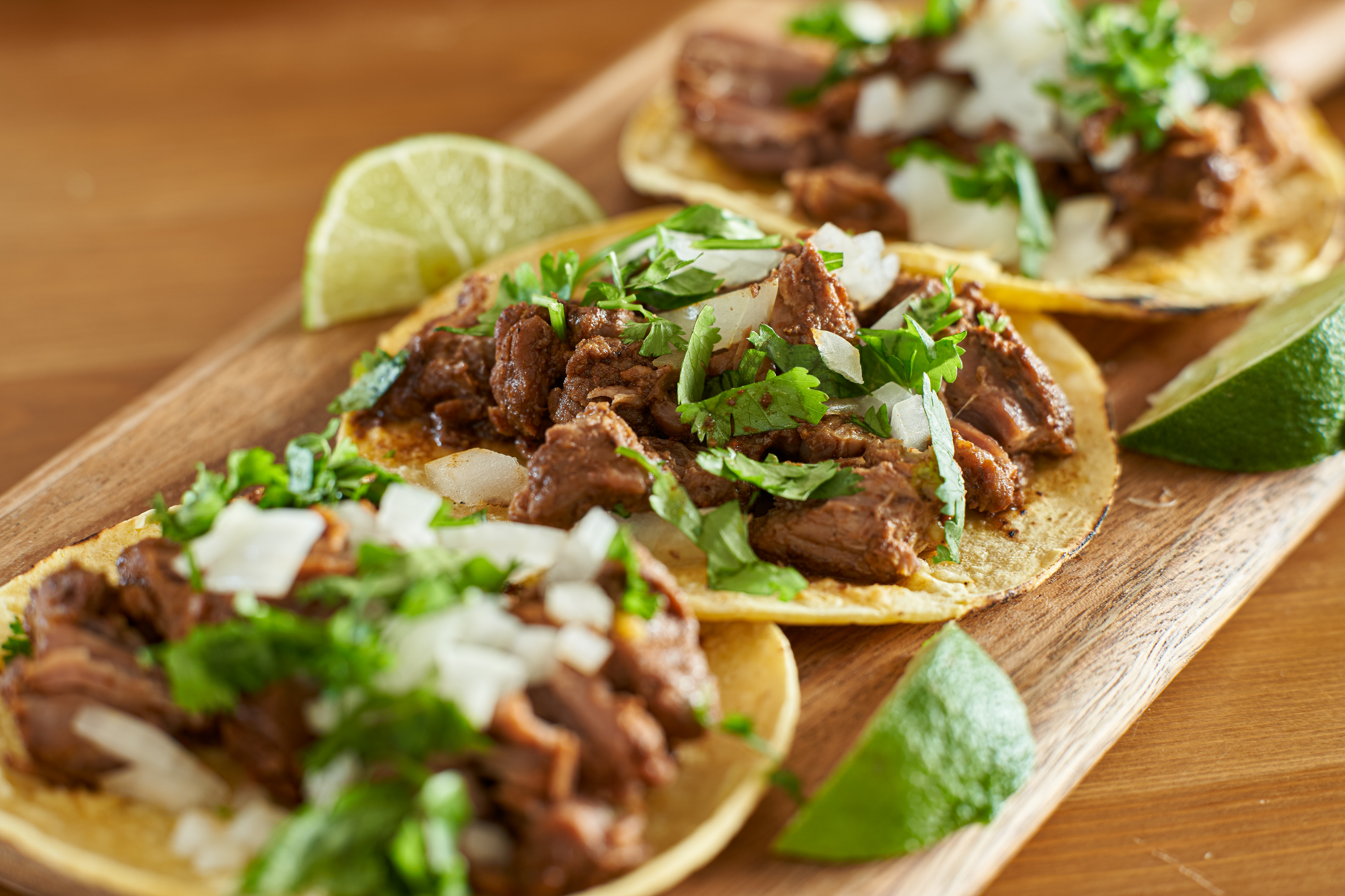 Three carne asada Mexican street tacos in corn tortilla with lime close up.